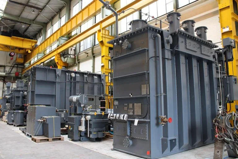 Large gray industrial transformers stand inside a warehouse.