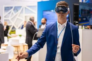 A man in a blue suit wears a virtual reality headset.